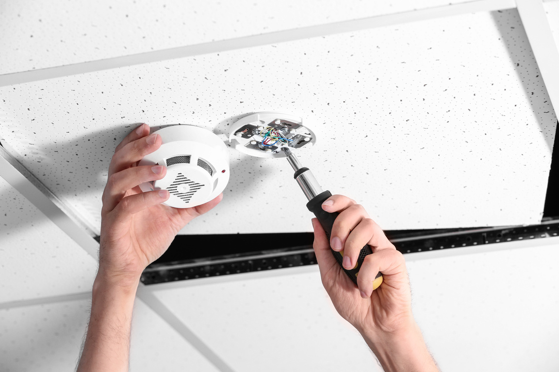 Young Male Technician Installing Smoke Alarm System Indoors